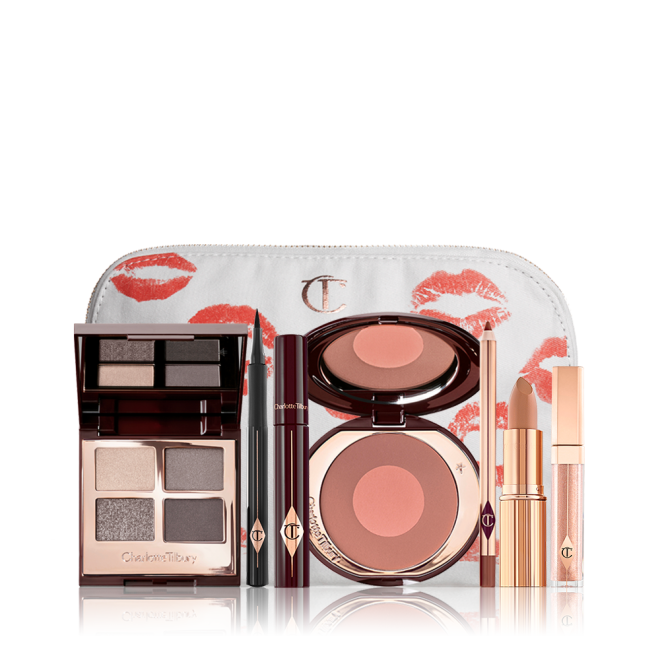 A white-coloured makeup pouch with an open two-tone blush in cool-toned brown and rose gold with a mascara, eyeliner pen, quad eyeshadow palette with shimmery and matte grey, beige and silver shades, an open lipstick in nude red, lip liner pencil in taupe-brown, and a lip gloss in nude pink. 