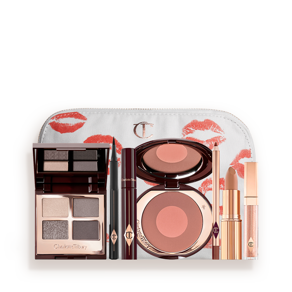 A white-coloured makeup pouch with an open two-tone blush in cool-toned brown and rose gold with a mascara, eyeliner pen, quad eyeshadow palette with shimmery and matte grey, beige and silver shades, an open lipstick in nude red, lip liner pencil in taupe-brown, and a lip gloss in nude pink. 
