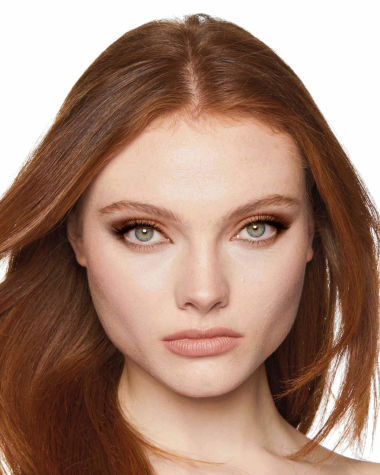 A fair-tone model with grey eyes wearing nude pink lipstick with matte eye makeup in shades of light brown, dark brown, and peach. 