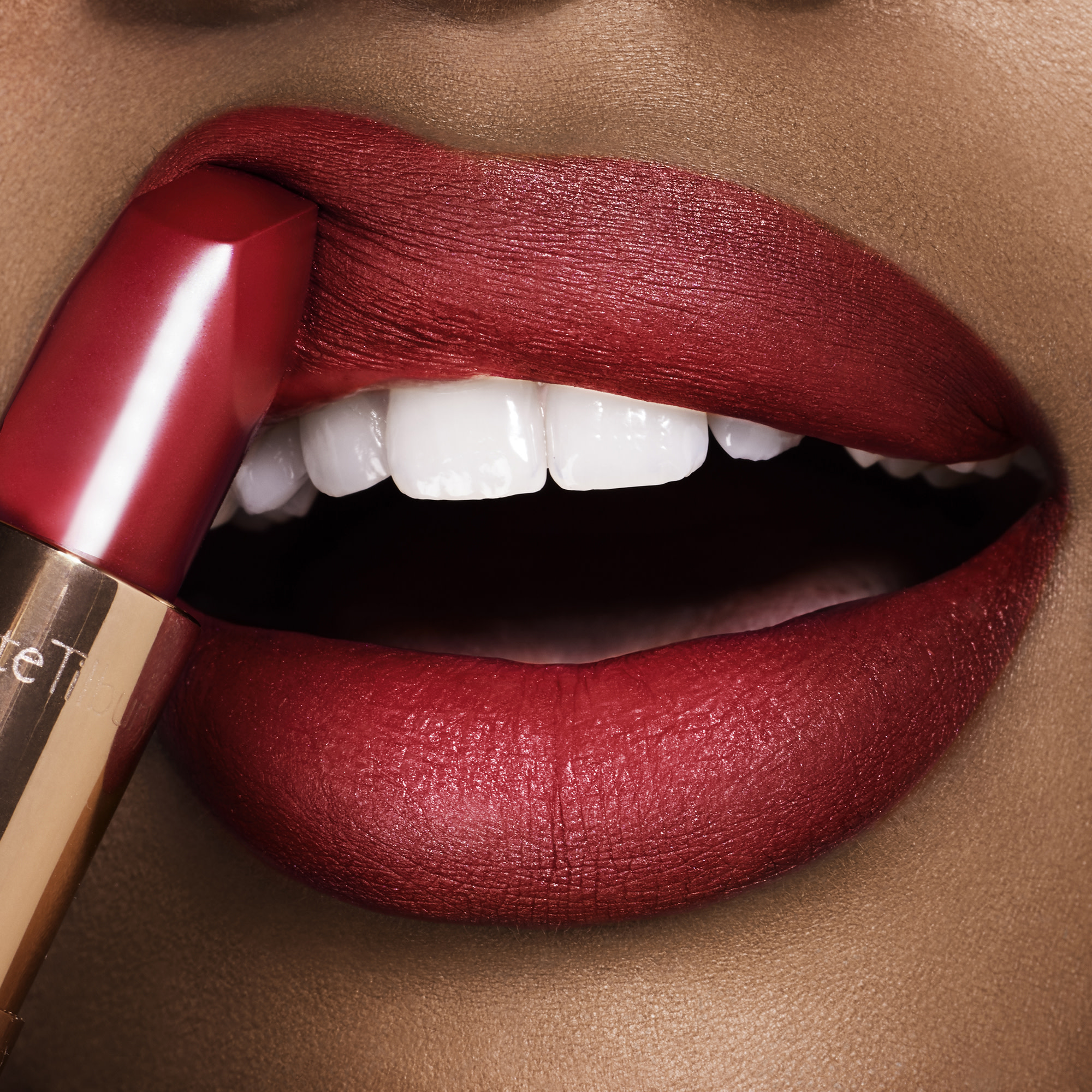 Lips close-up of a deep-tone model applying a soft, neutral wine-coloured lipstick with a matte finish.