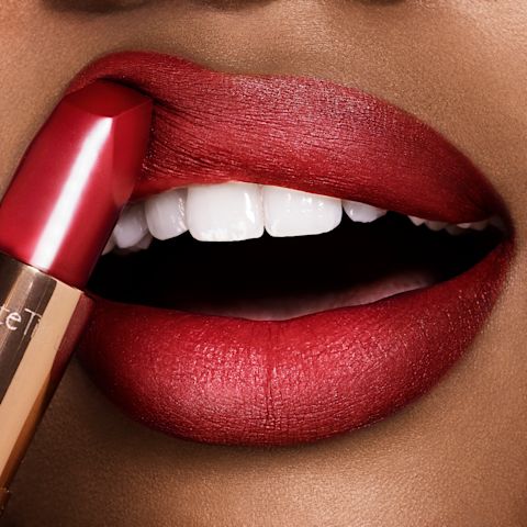 Lips close-up of a deep-tone model applying a soft, neutral wine-coloured lipstick with a matte finish.