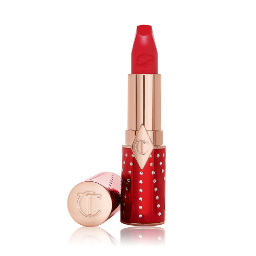 An open lipstick in a matte, bright cherry red shade in a red and gold-coloured tube.