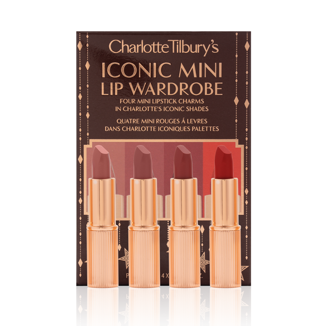 Five matte lipsticks in nude shades of red and pink in sleek, gold-coloured tubes with their dark-brown gift set box behind them with text written on the front that reads, 'Charlotte Tilbury's Iconic mini lip wardrobe'.