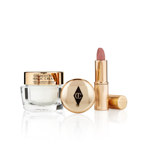 Pearly-white face cream in a glass jar with a gold-coloured lid, a closed pressed powder compact in reflective gold-coloured packaging, and a dusky pink lipstick in a sleek gold-coloured tube.