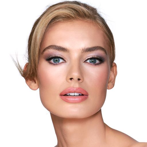 A light-tone blonde model with blue eyes wearing shimmery lilac and champagne eye makeup with nude pink blush and a warm, coral lipstick. 