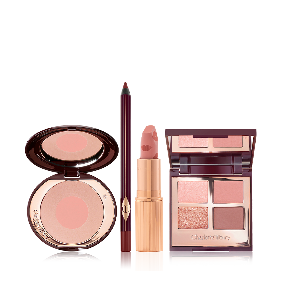 An open, two-tone blush compact in nude pink and champagne, eyeliner in berry-brown, open lipstick in muted pink, and quad eyeshadow palette with matte and shimmery shades of pink, gold, and brown with a mirrored-lid.