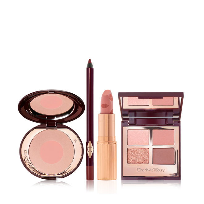 An open, two-tone blush compact in nude pink and champagne, eyeliner in berry-brown, open lipstick in muted pink, and quad eyeshadow palette with matte and shimmery shades of pink, gold, and brown with a mirrored-lid.