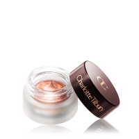 An open glass pot filled with shimmery cream eyeshadow in rose-gold shade with its lid next to it. 