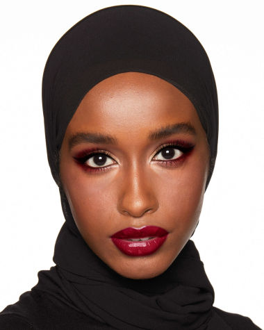 A deep-tone brunette model with reddish-plum eye makeup, glowy face base, and a vampy-red lipstick with a satin-finish. 