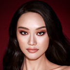 A fair-tone model with brown eyes wearing smokey brown and gold eye makeup with warm pink blush and glossy nude-pink lips.