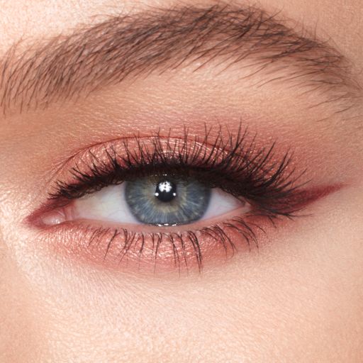 A close-up of a blue-eyed, fair skin model wearing a berry-brown eyeliner with glowy, peach eye makeup. 