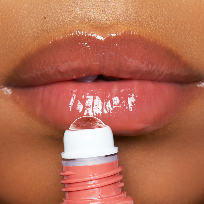 Lips close-up of a deep-tone model applying an orange coral, high-shine lip oil.  