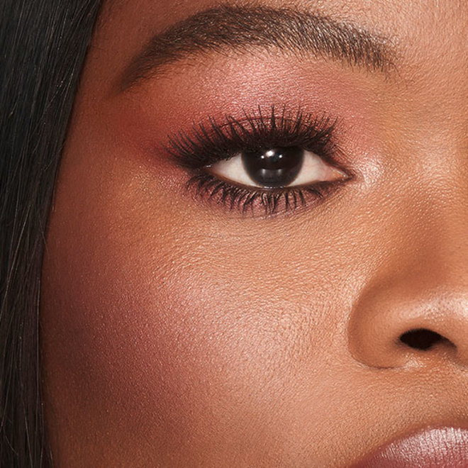 Deep-tone model with brown eyes wearing berry-pink shimmery eye makuep with a berry-rose blush with champagne undertones.