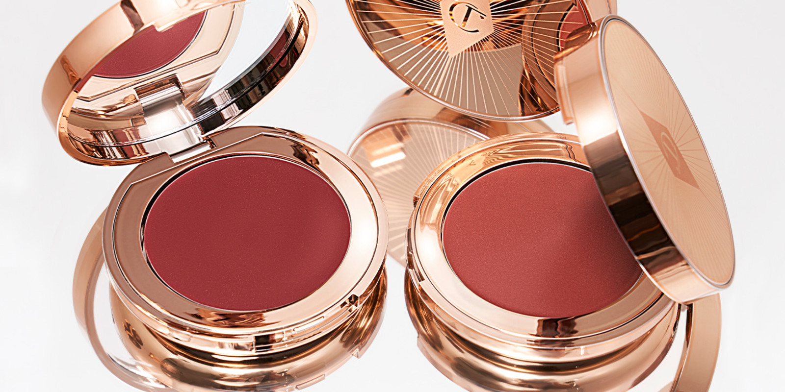 A collection of lip and cheek cream compacts in gold packaging in shades of berry-pink and rosebud pink. 