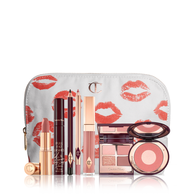 A mascara with an open, mirrored-lid quad eyeshadow palette in shimmery neutral shades, a shimmery nude pink lipstick, a nude pink lip gloss and lip liner pencil, and a two-tone powder blush compact in a bright pink shade, with all products in front of a white-coloured makeup pouch. 