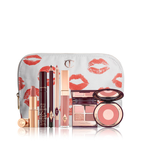 A mascara with an open, mirrored-lid quad eyeshadow palette in shimmery neutral shades, a shimmery nude pink lipstick, a nude pink lip gloss and lip liner pencil, and a two-tone powder blush compact in a bright pink shade, with all products in front of a white-coloured makeup pouch. 