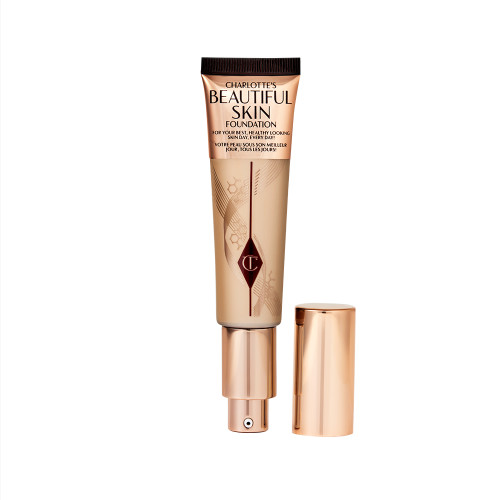 An open foundation wand in gold packaging with a pump dispenser and a medium-beige-coloured body to show the shade of the foundation inside. 