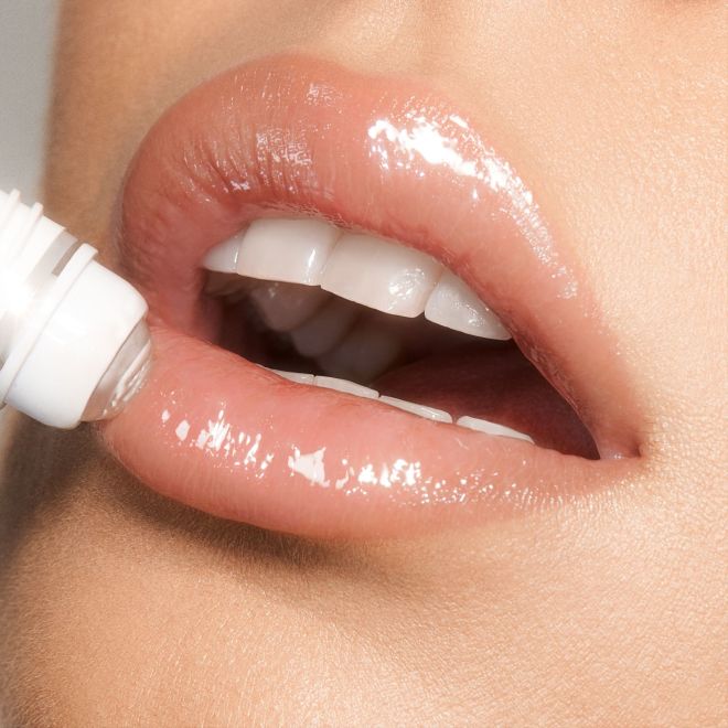 Close-up of a light-tone model applying a nourishing, clear lip oil with a crystal roller ball applicator. 