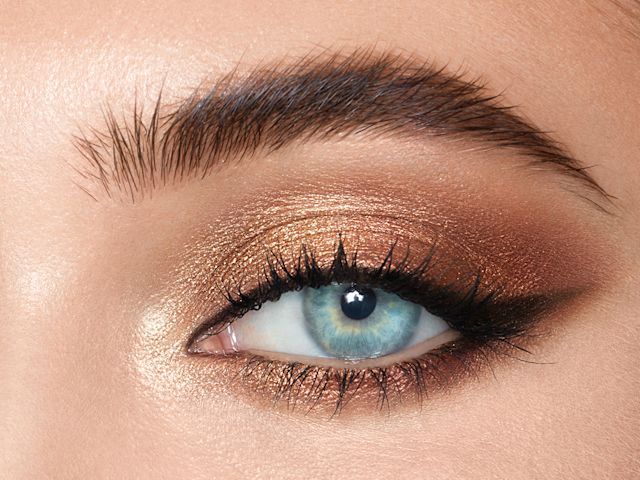 Close-up of a light-tone model's blue eye with shimmery gold, bronze, and champagne eye makeup. 