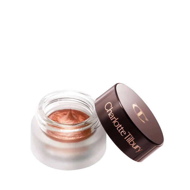 An open glass pot with shimmery russet rose cream eyeshadow with golden-peach sparkle and its lid placed next to it.