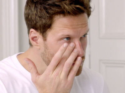 A fair-tone male model patting a skincare product on his face. 