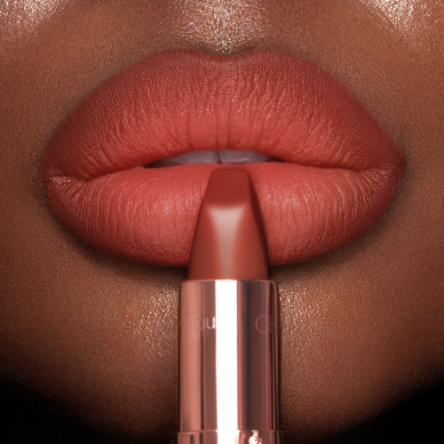 Lips close-up of a deep-tone model wearing a matte, burnt-orange red lipstick.