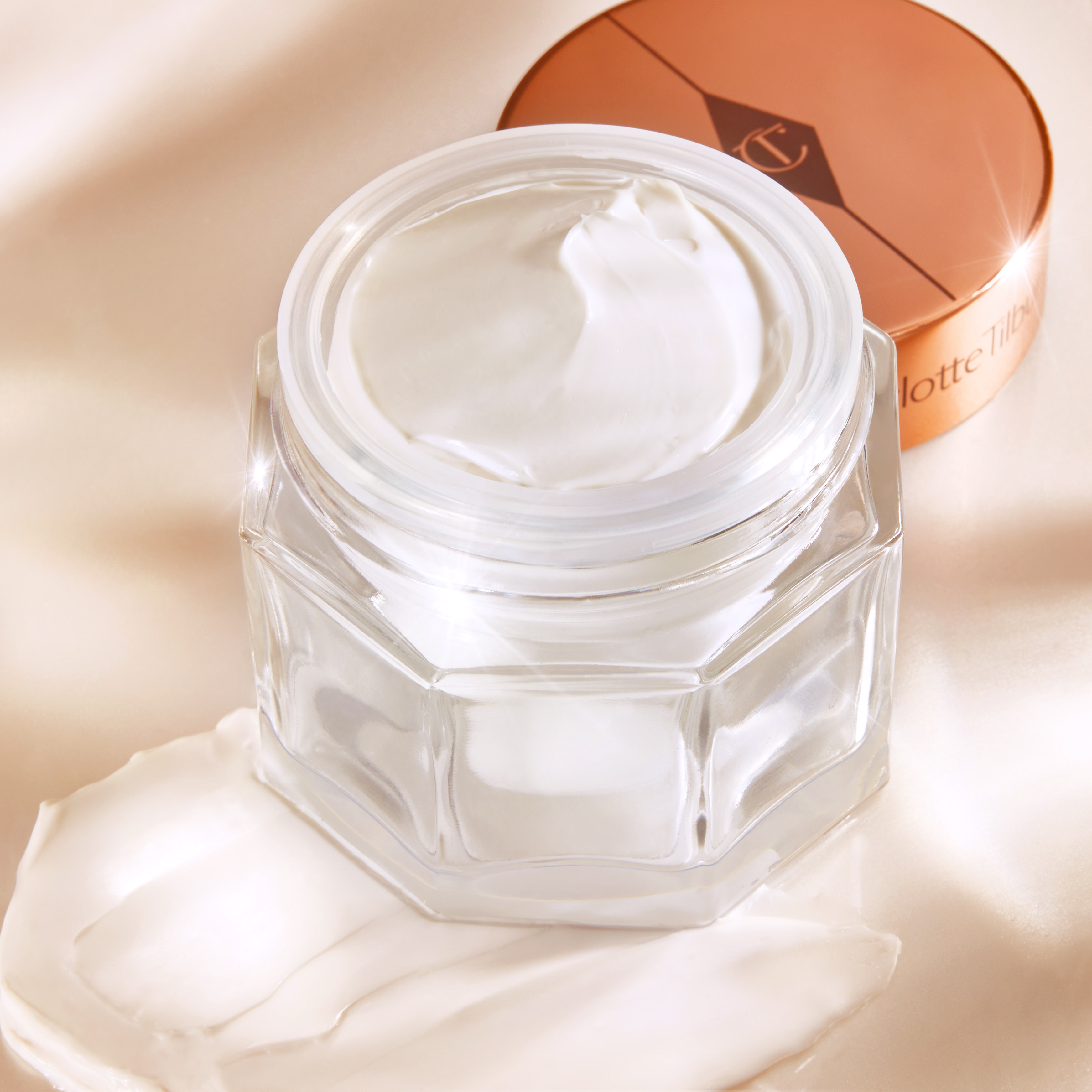 Thick and luscious pearly-white moisturiser in an open glass jar with its gold-coloured lid placed behind it. swatch for winter skincare routine blog