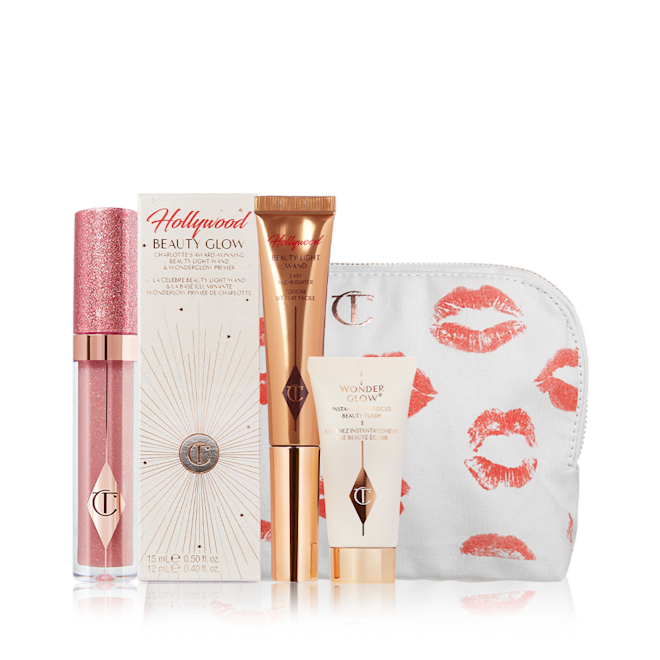 Hollywood Glow Icons displayed Nude pink shimmery lip gloss in a glass tube, glowy primer in a white-coloured box, liquid highlighter wand in a bronze-gold-coloured tube, and a white-coloured makeup pouch with kiss prints all over.