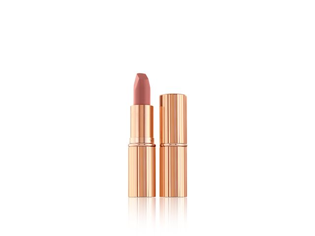 A closed matte lipstick with an open one in a nude-pink matte shade, both in metallic, golden-coloured packaging. 