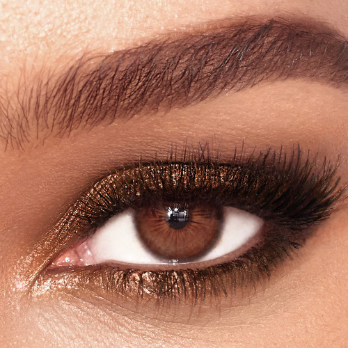 Single-eye close-up of a brown-eyed model wearing shimmery amber-coloured eyeshadow. 