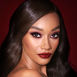 A deep-tone model with brown eyes wearing reddish-plum eye makeup, glowy face base, and a vampy-red lipstick with a satin-finish. 