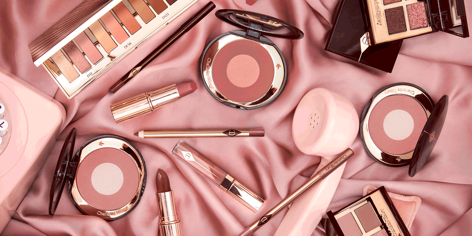 A collection of different makeup products that include lip gloss, lipstick, lip liner pencils, eyeliner pencil, lipstick lip balm, two-tone blush compacts, 12-pan and quad eyeshadow palettes in berry pink, nude pink, dark brown-pink colours. 