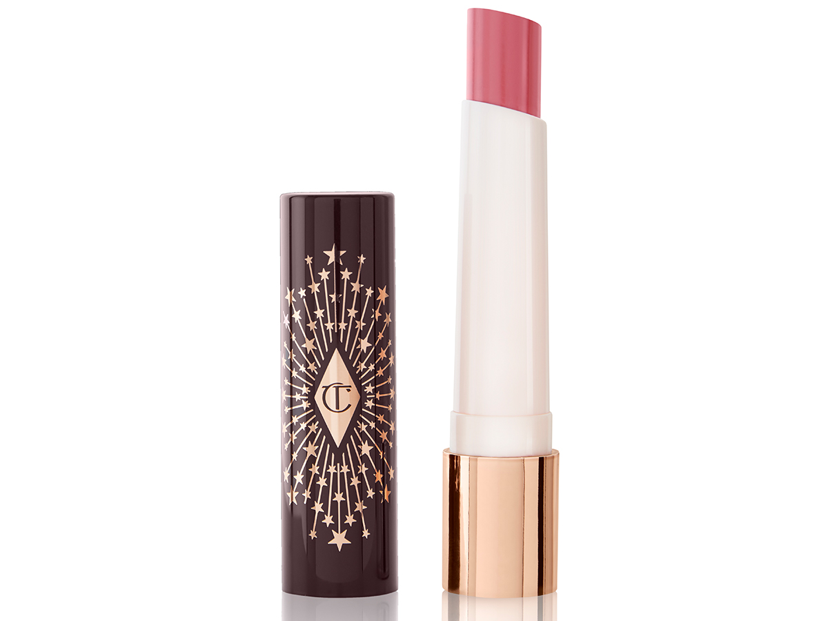An open lipstick lip balm in a sheer nude pink berry shade, in white and gold tube with a black-coloured lid with gold sparkles all over it.
