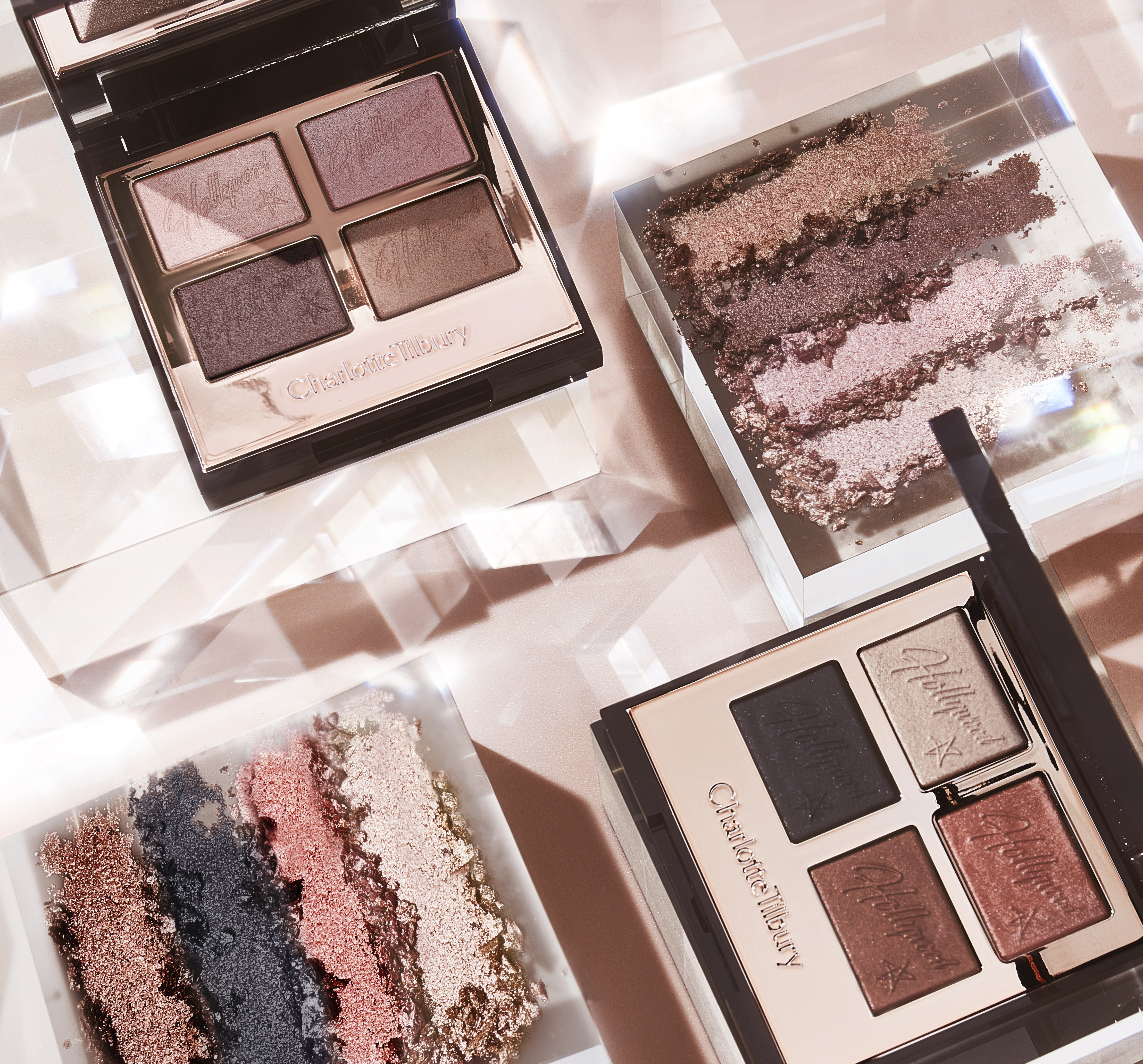 Two, open mirrored-lid quad eyeshadow palettes. One with shimmery and matte eyeshadows in pink champagne, metallic blush pink, mink brown and antiqued brown colours, and the other with matte and shimmery eyeshadows in rose gold, chocolate brown, champagne, and black.