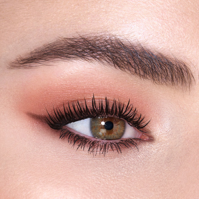 Single-eye close-up of a fair-tone model with green eyes wearing smokey peach eyeshadow. 