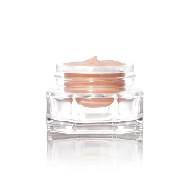 A petite, open glass jar with a dark champagne-coloured eye cream. 