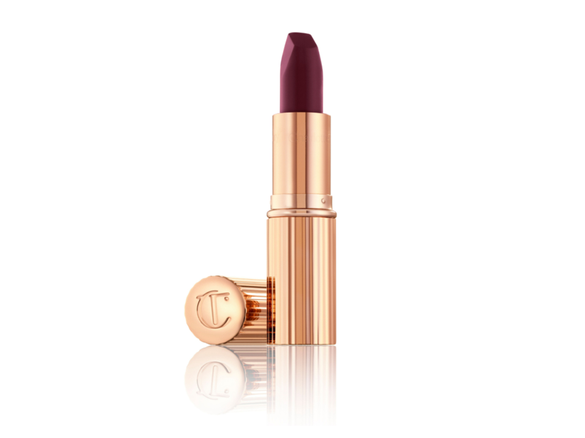 An open, deep purple berry matte lipstick in a gold-coloured tube with its lid next to it.