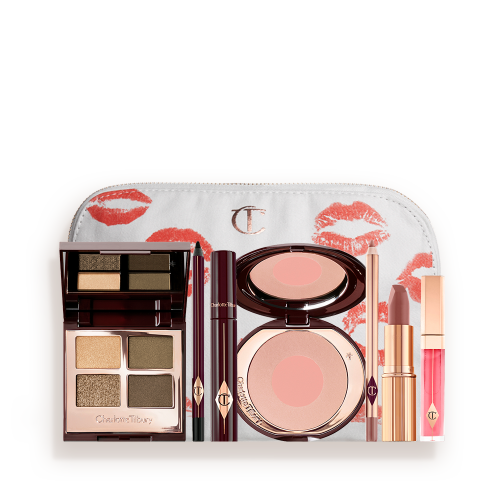 A white makeup bag with a quad eyeshadow palette in shades of green and gold, a brown eyeliner pencil, mascara, an open two-tone blush in nude pink, a warm pink lip liner pencil, a warm rose lipstick, and a bright pink lip gloss. 