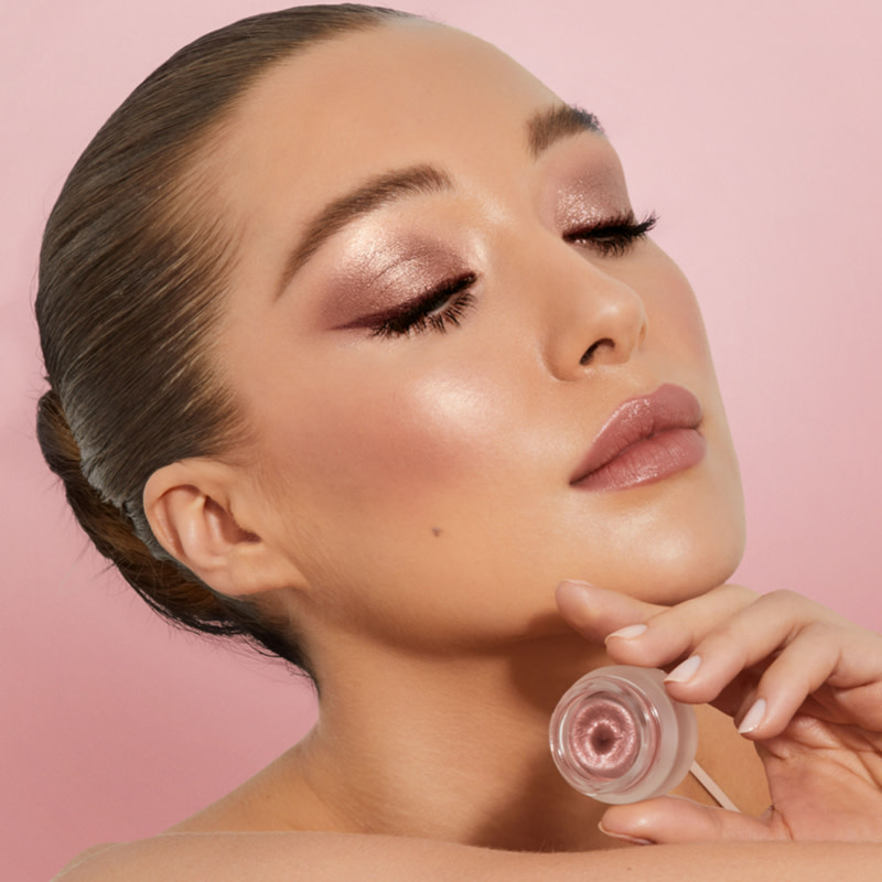 Light-tone brunette model wearing a metallic, rose-coloured cream eyeshadow with soft mauve lipstick topped with lip gloss, and glowy rose-gold blush.