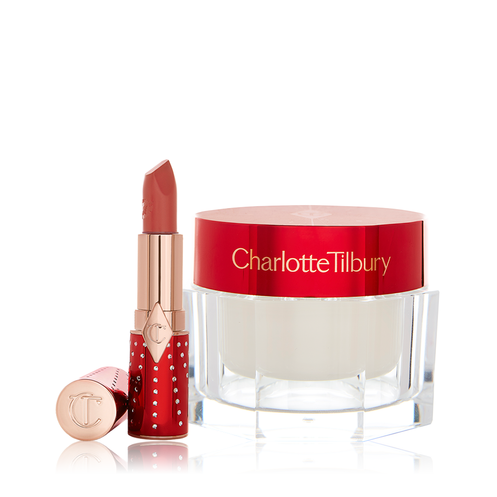 An open lipstick in red and gold packaging in a dark brown-peach shade with a face cream in a pearly-white colour in a glass jar with a red-coloured lid. 