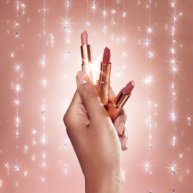 Mini Lipstick collection held by medium-tone model Close-up of a medium-tone model's hand holding three mini open lipsticks in nude pink, brown-pink, and statement red.