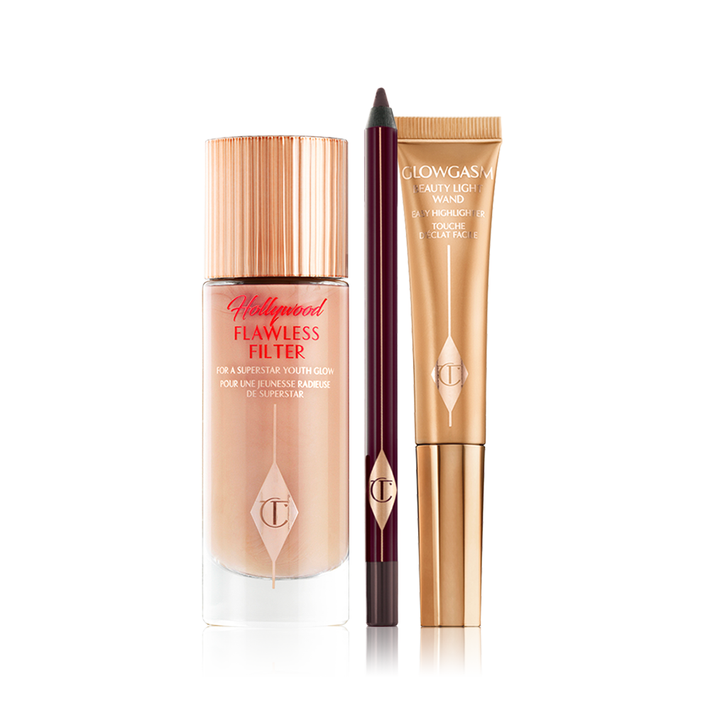 A luminous, champagne-coloured creamy primer in a glass bottle, an open kohl liner pencil in dark brown, and a highlighter wand in a warm golden-coloured packaging. 