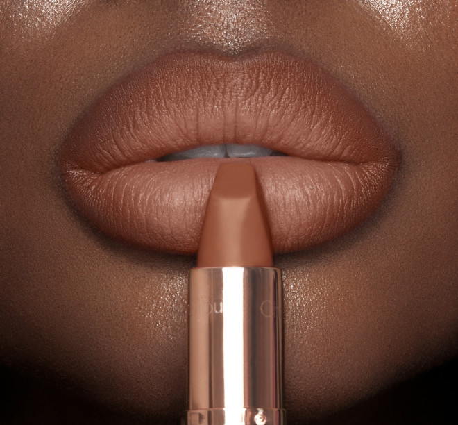 Lips close-up of a deep-tone model wearing a fresh, neutral nude peach lipstick with a matte finish.