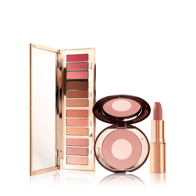 An open, mirrored-lid eyeshadow palette with matte and shimmery nude shades, a two-tone powder blush in nude pink, and a nude pink lipstick in a golden-coloured tube. 