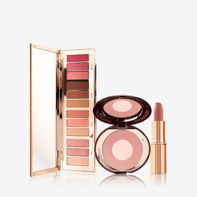 Instant Pillow Talk Glow Kit open An open, mirrored-lid eyeshadow palette with matte and shimmery nude shades, a two-tone powder blush in nude pink, and a nude pink lipstick in a golden-coloured tube.