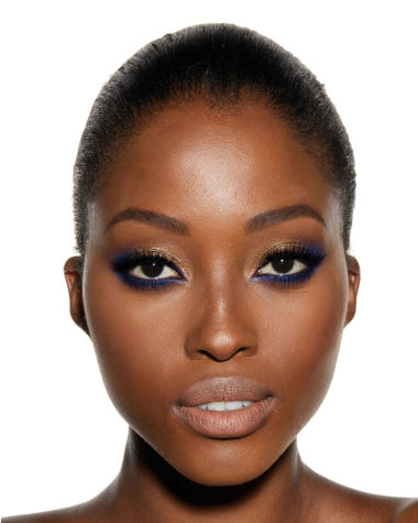 A deep-tone brunette model with brown eyes with shimmery gold and royal blue eyeshadow with matte and metallic eyeliner in royal blue on the upper eyelid and lower waterline. 