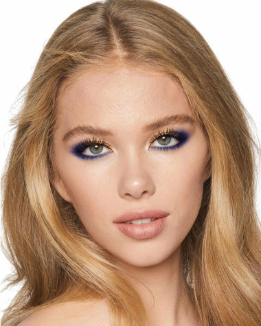 A light-tone model with blonde hair and blue eyes with shimmery gold and royal blue eyeshadow with matte and metallic eyeliner in royal blue on the upper eyelid and lower waterline. 