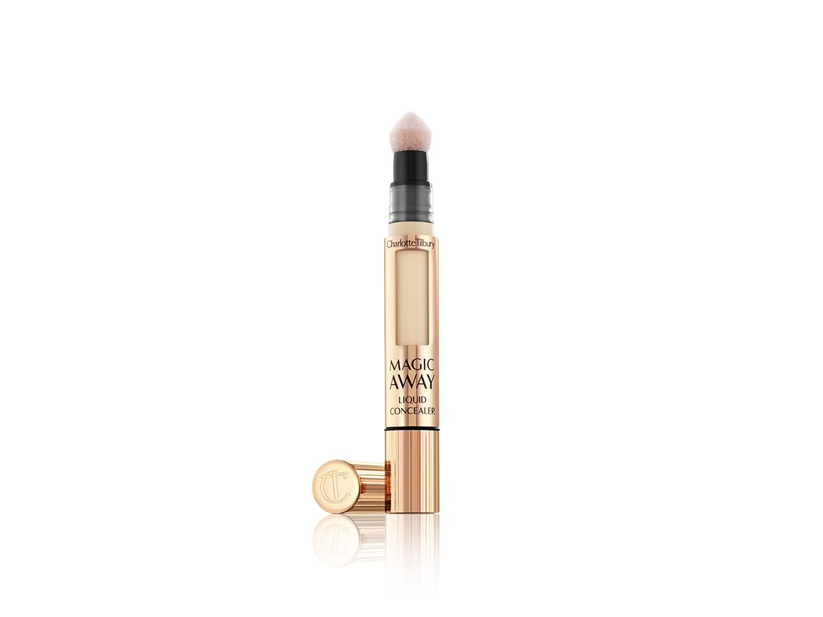 A concealer in a fair shade in golden-coloured packaging with its lid next to it. 