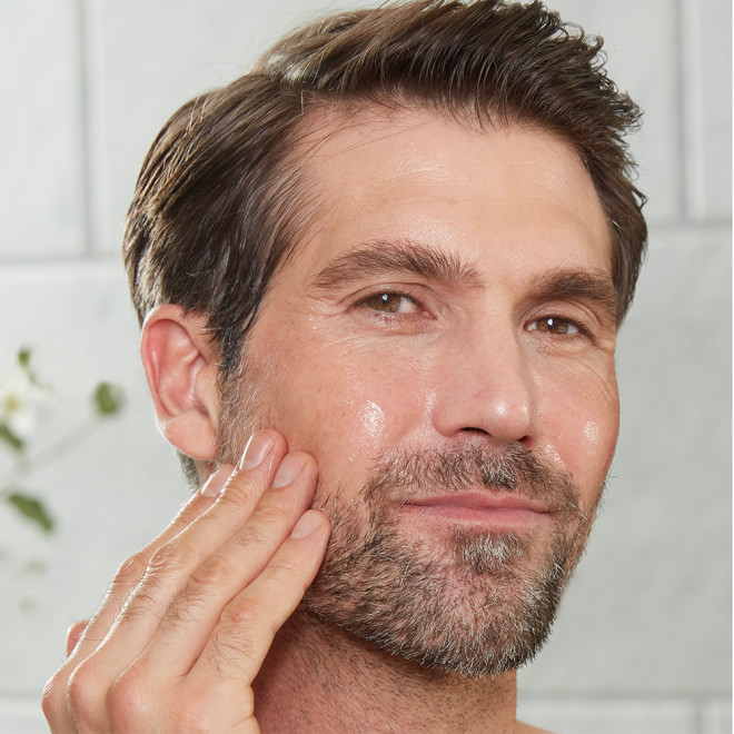 A light-tone male model with mature yet glowy, smooth, and radiant skin washing off an exfoliating mask.