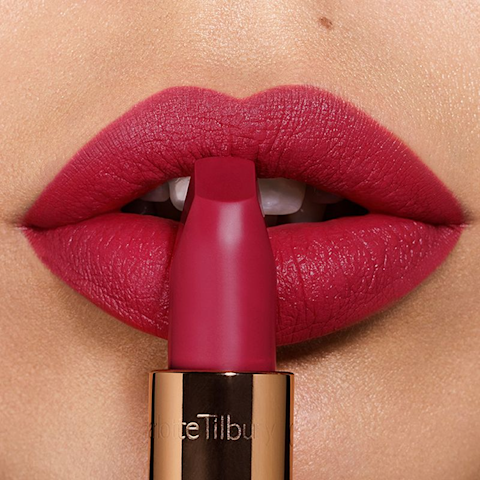 Lips close-up of a light-tone model wearing a rosy jewel-inspired pink matte lipstick while holding the lipstick in front of her lips.